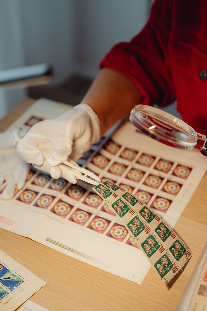 A philatelist using a magnifying glass to inspect a stamp collection indoors.