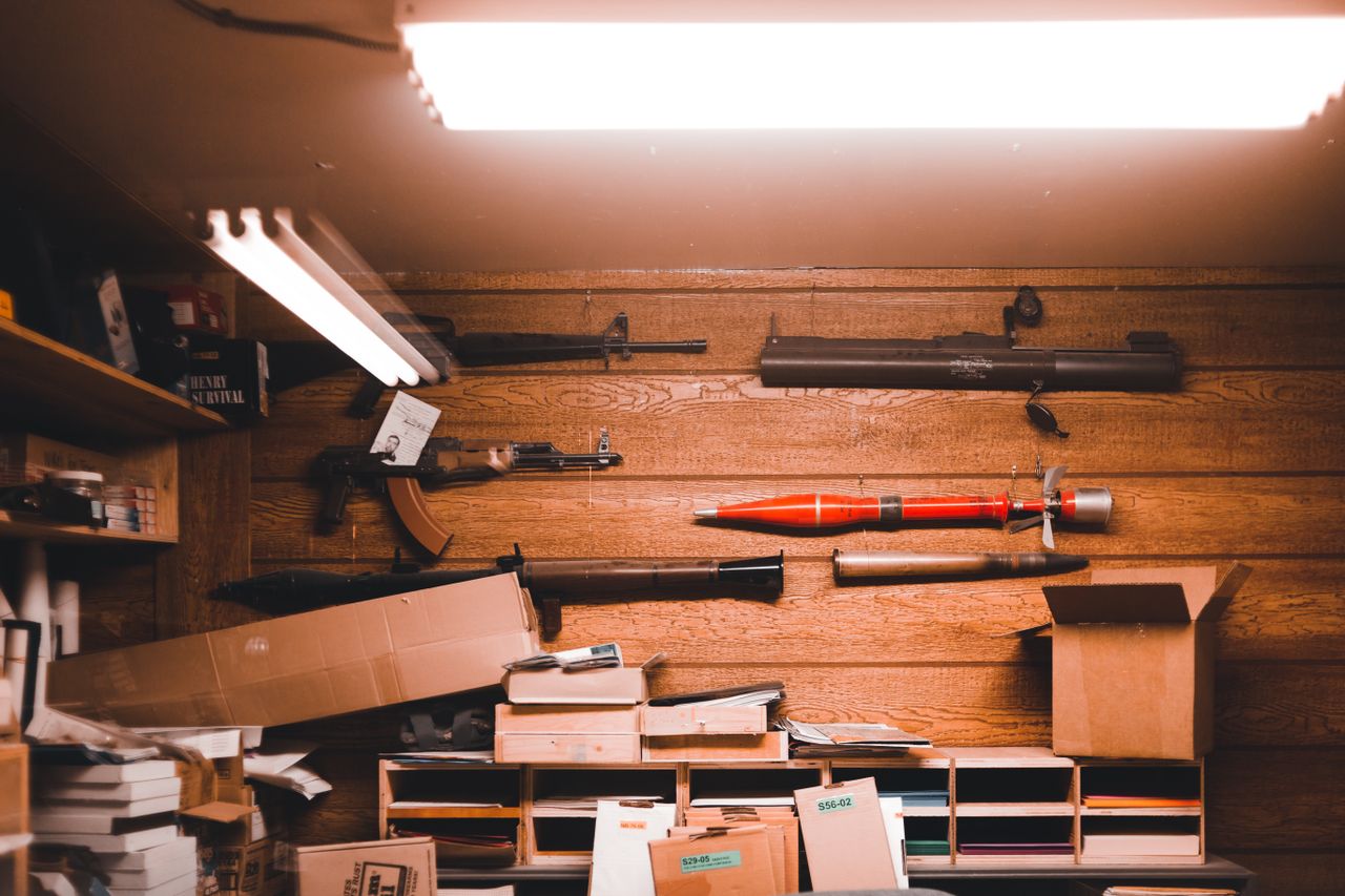 Interior of an armory with wooden walls, weapons, and equipment stored in boxes.